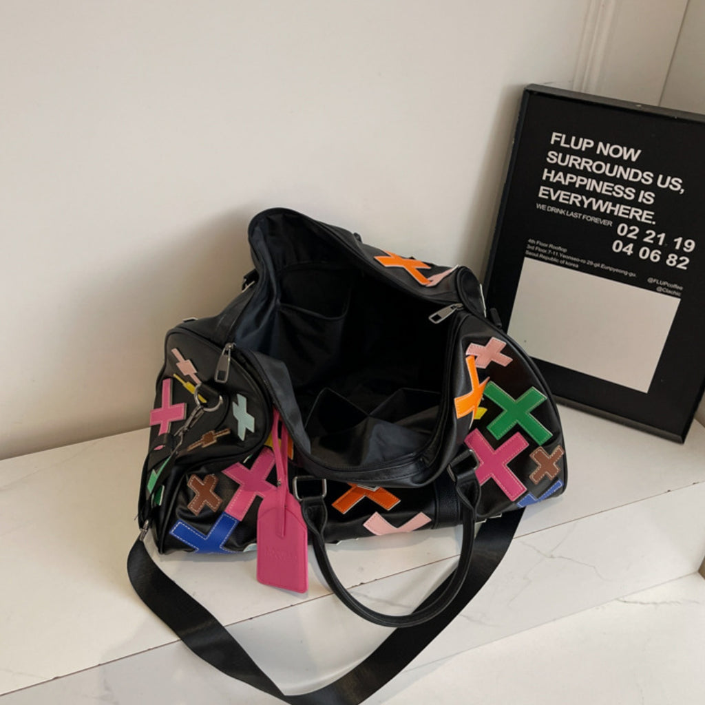 Black duffel bag with colorful patterns on a white surface next to a framed text piece.