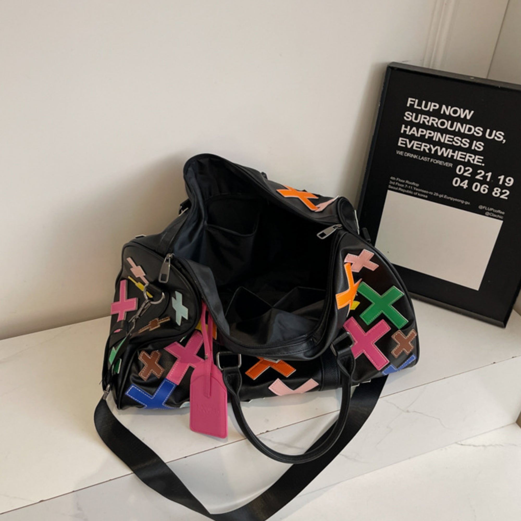 Black duffel bag with colorful patterns on a white surface next to a framed text piece.