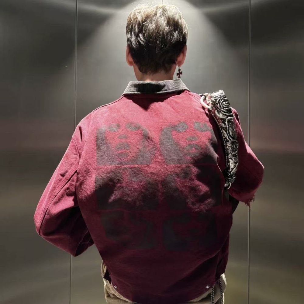 Person wearing a red jacket with 'BC' on the back, standing in front of a reflective surface.