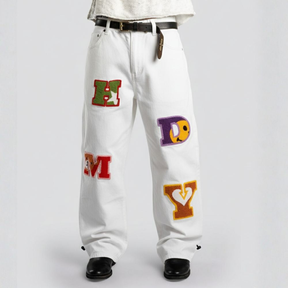 White jeans with colorful letter patches on a plain background
