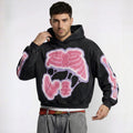 Man wearing a black hoodie with pink and white graphic design on a plain background