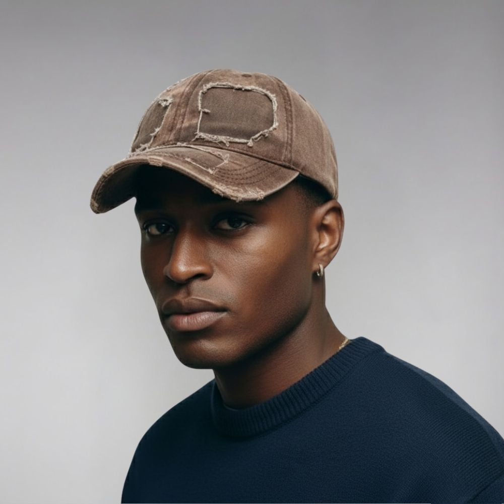 Man wearing a brown distressed baseball cap against a gray background