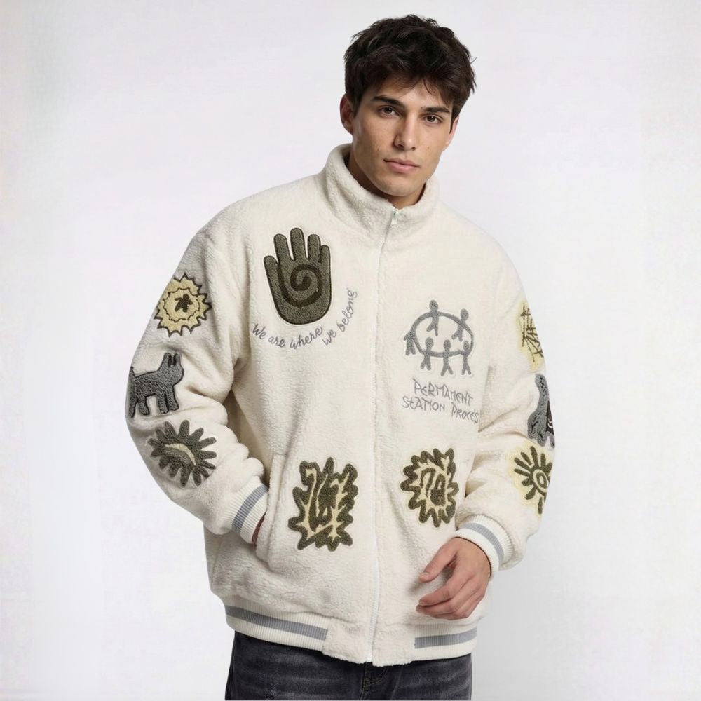 Man wearing a cream-colored jacket with decorative patterns on a white background