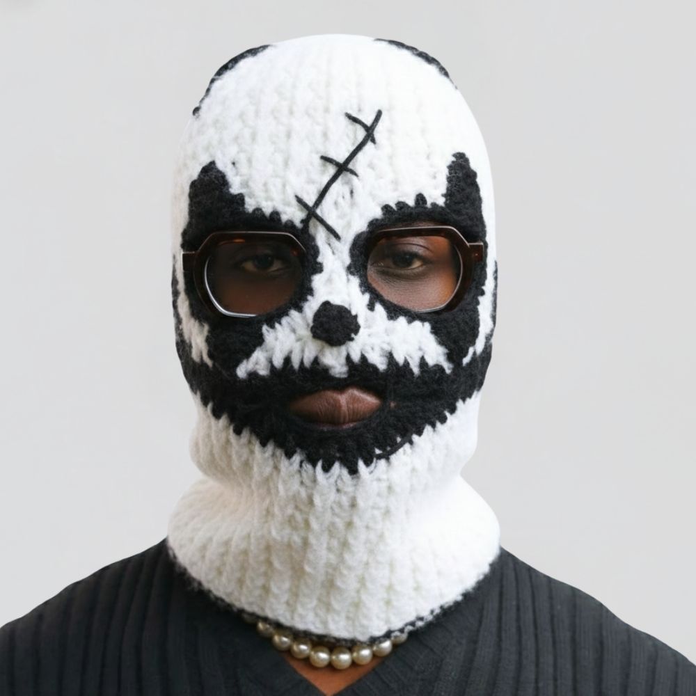 Person wearing a black and white knitted balaclava with a skull design on a gray background